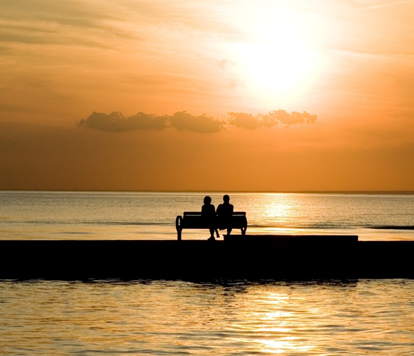 夕陽西下一對情侶坐在海邊長椅欣賞美景